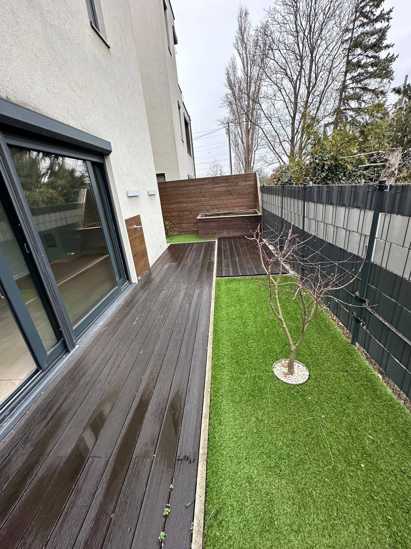 Moderne Holzterrasse mit Kunstrasenfläche und Zugang zum Innenbereich des Hauses.