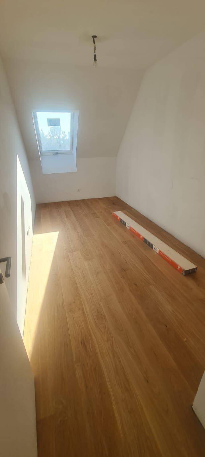 Helles Zimmer im Dachgeschoss mit Holzparkettboden und einem Dachfenster.
