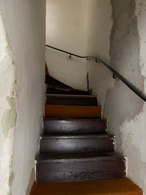 Treppenhaus mit abgenutzten Holzstufen und einem einfachen Handlauf, der nach oben führt.