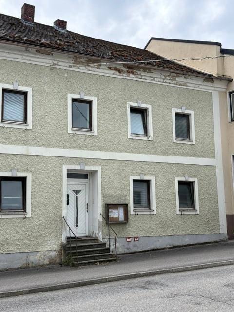 Nahaufnahme der Fassade eines älteren Gebäudes mit sichtbaren Gebrauchsspuren und Fenstern.