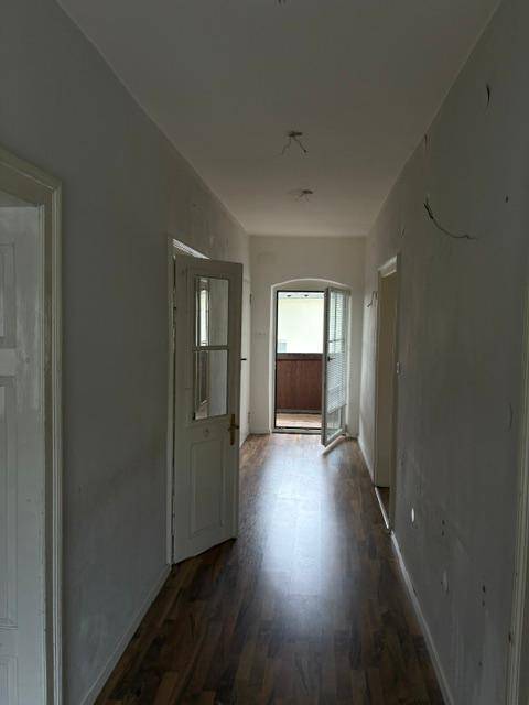 Heller Flur mit Laminatboden und Zugang zu einem Balkon, der Tageslicht hereinlässt.