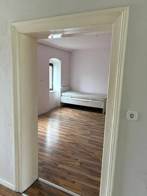 Blick durch eine Tür in ein Schlafzimmer mit Bett, rosa Wänden und Laminatboden.