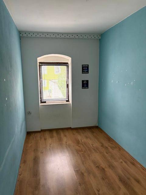 Kleines Zimmer mit blauen Wänden, einem Fenster und Laminatboden, ideal als Kinderzimmer.
