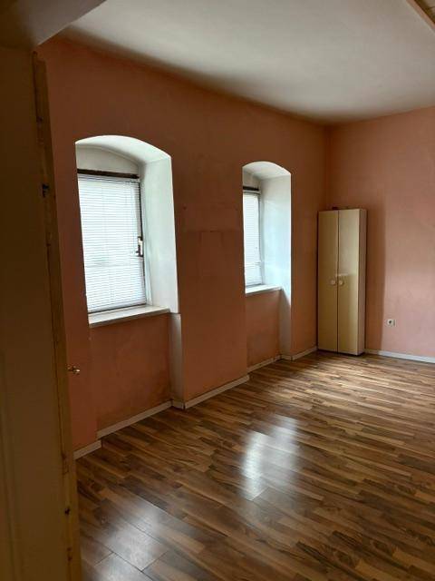 Schlafzimmer mit rosa Wänden, zwei gewölbten Fenstern und Laminatboden, inklusive Kleiderschrank.