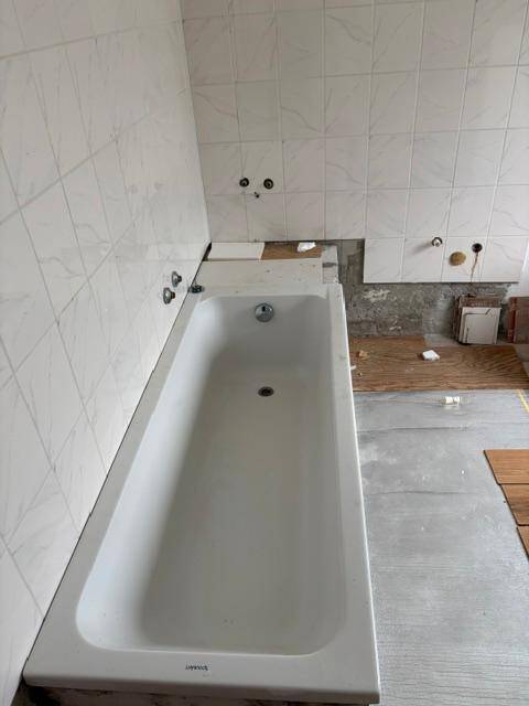 Badewanne in einem Badezimmer, das sich im Umbau befindet, mit teilweise gefliesten Wänden.