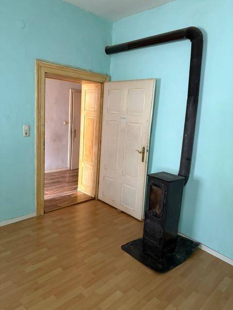 Wohnraum mit Holzofen und Laminatboden, blaue Wände und offener Zugang zu einem weiteren Zimmer.