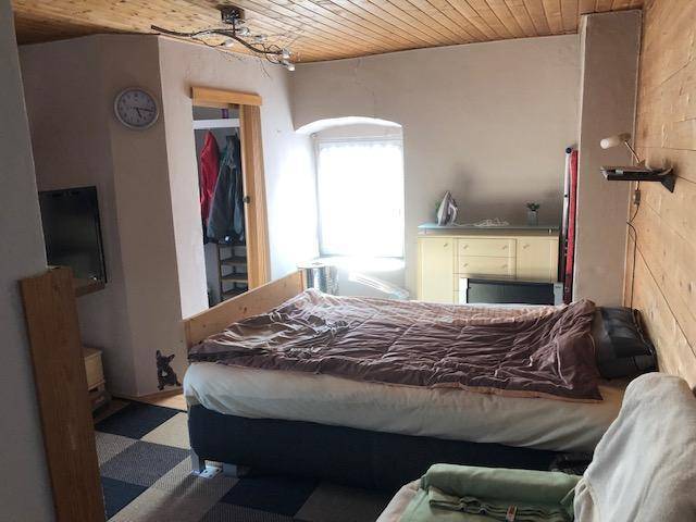 Gemütliches Schlafzimmer mit Holzbalkendecke, kariertem Fliesenboden und einem kleinen Fenster, das Tageslicht hereinlässt.