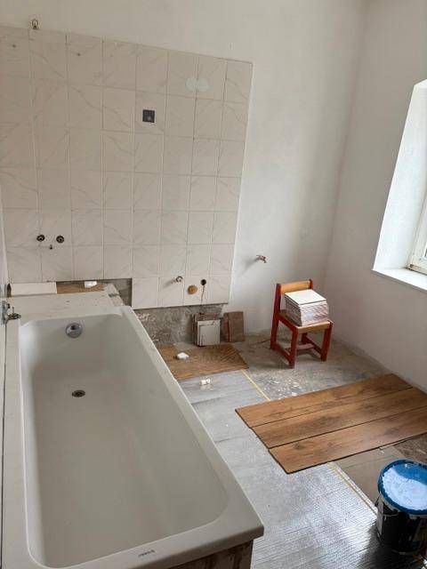 Badezimmer im Umbau mit installierter Badewanne, teilweise gefliesten Wänden und vorbereitetem Boden.