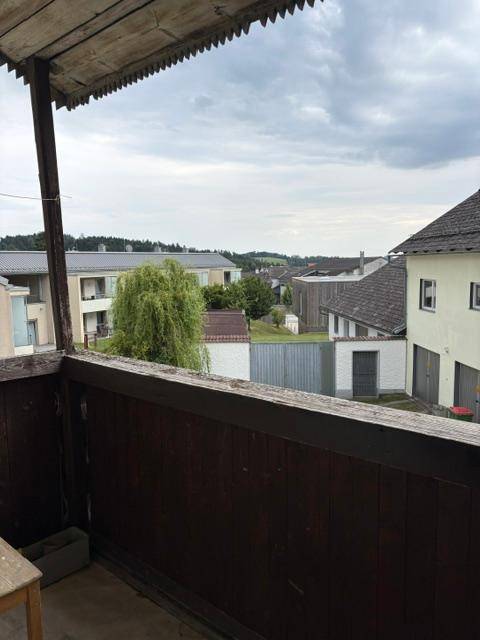 Balkon mit Blick auf eine Wohnsiedlung und grüne Bäume unter bewölktem Himmel.