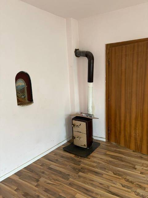 Heller Wohnraum mit einem Holzofen, weißen Wänden und Laminatboden, bereit zur Nutzung.