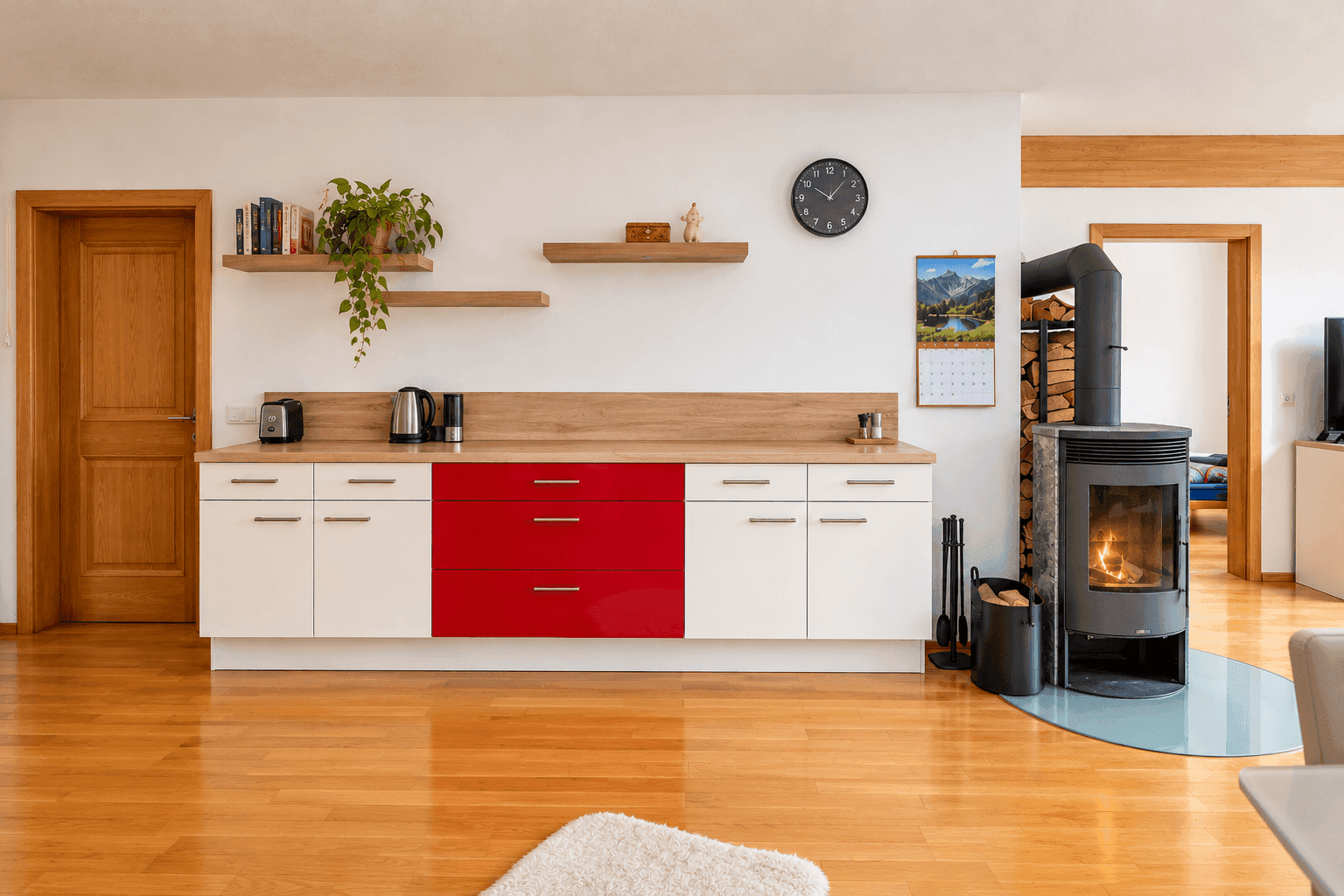 Offene Küche mit roten Akzenten und Kaminofen, integriert in den Wohnbereich mit Holzboden.