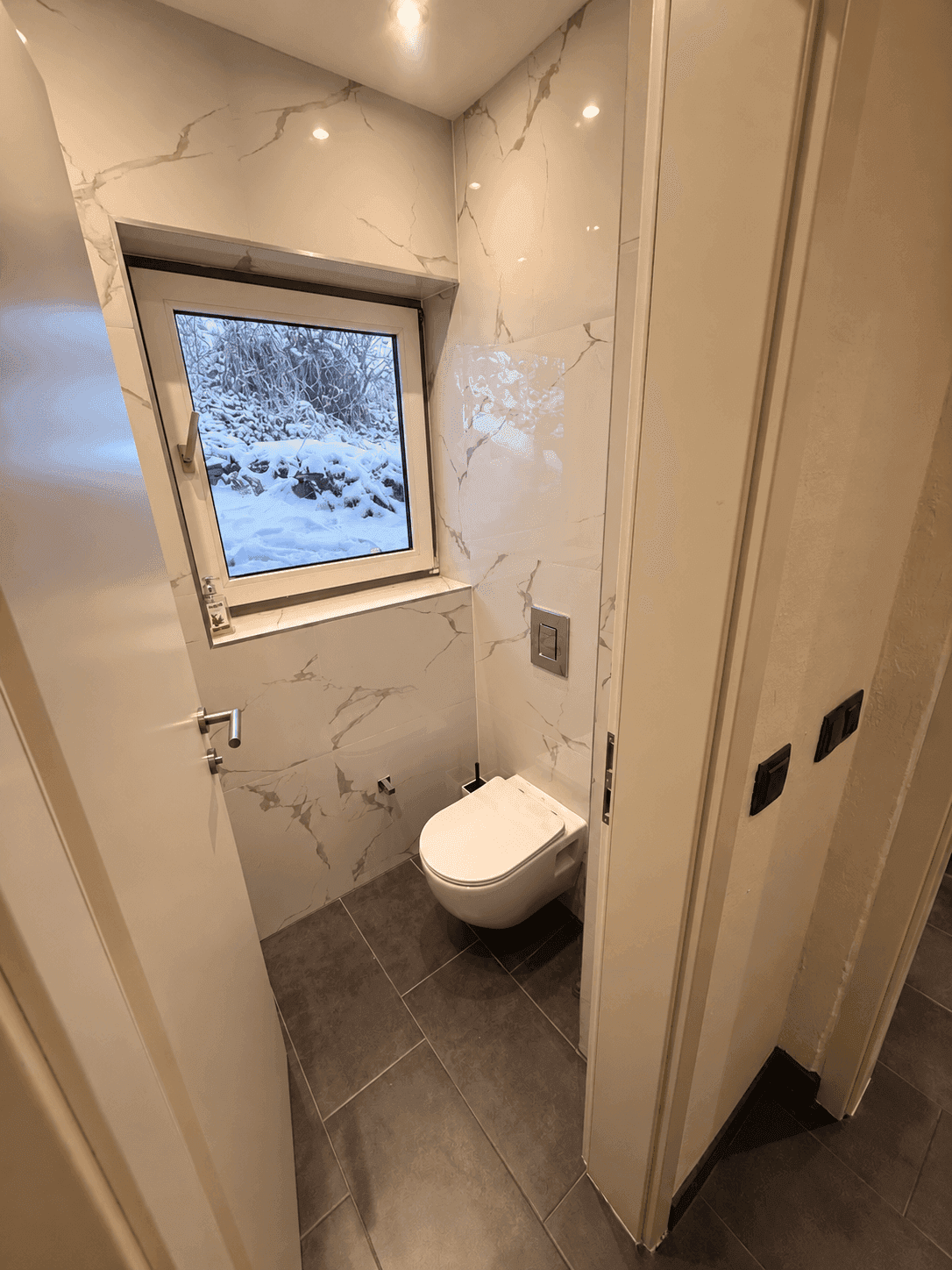 Modernes Gäste-WC mit Wand-WC, großformatigen Fliesen und Fenster für Tageslicht.