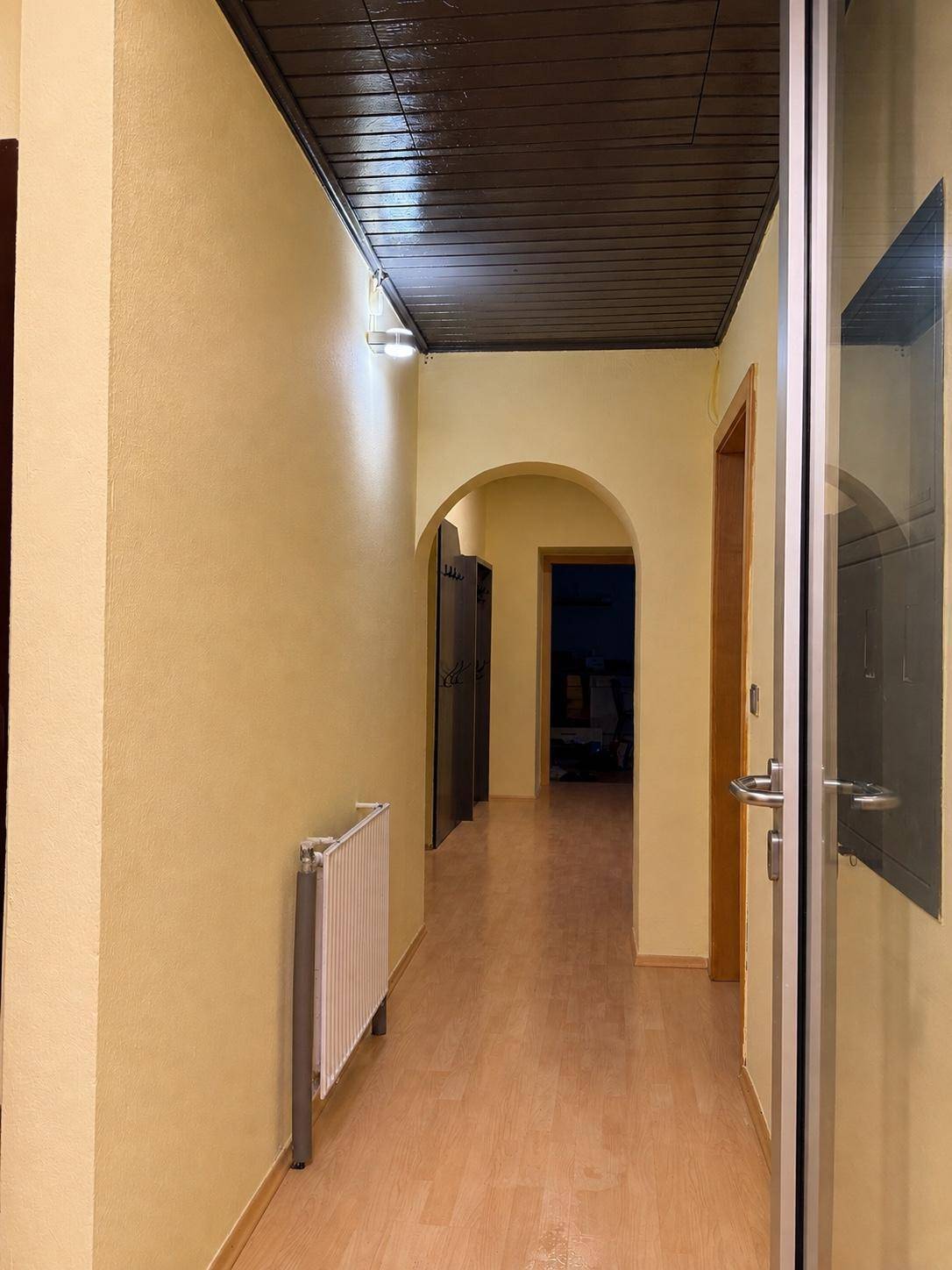 Langer Flur mit Holzboden, gelben Wänden und dunkler Holzdecke, führt zu weiteren Räumen.