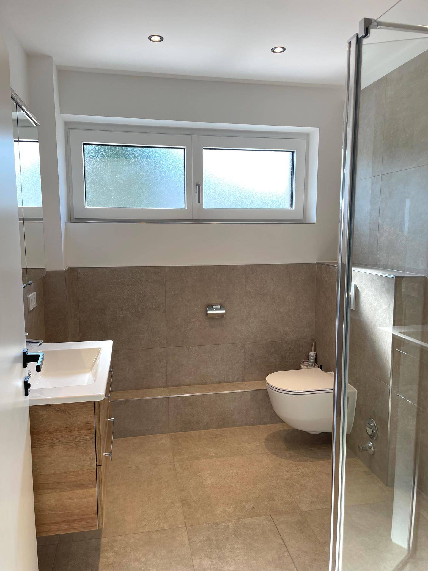 Modernes Badezimmer mit begehbarer Dusche, WC, Waschtisch und Fenster.