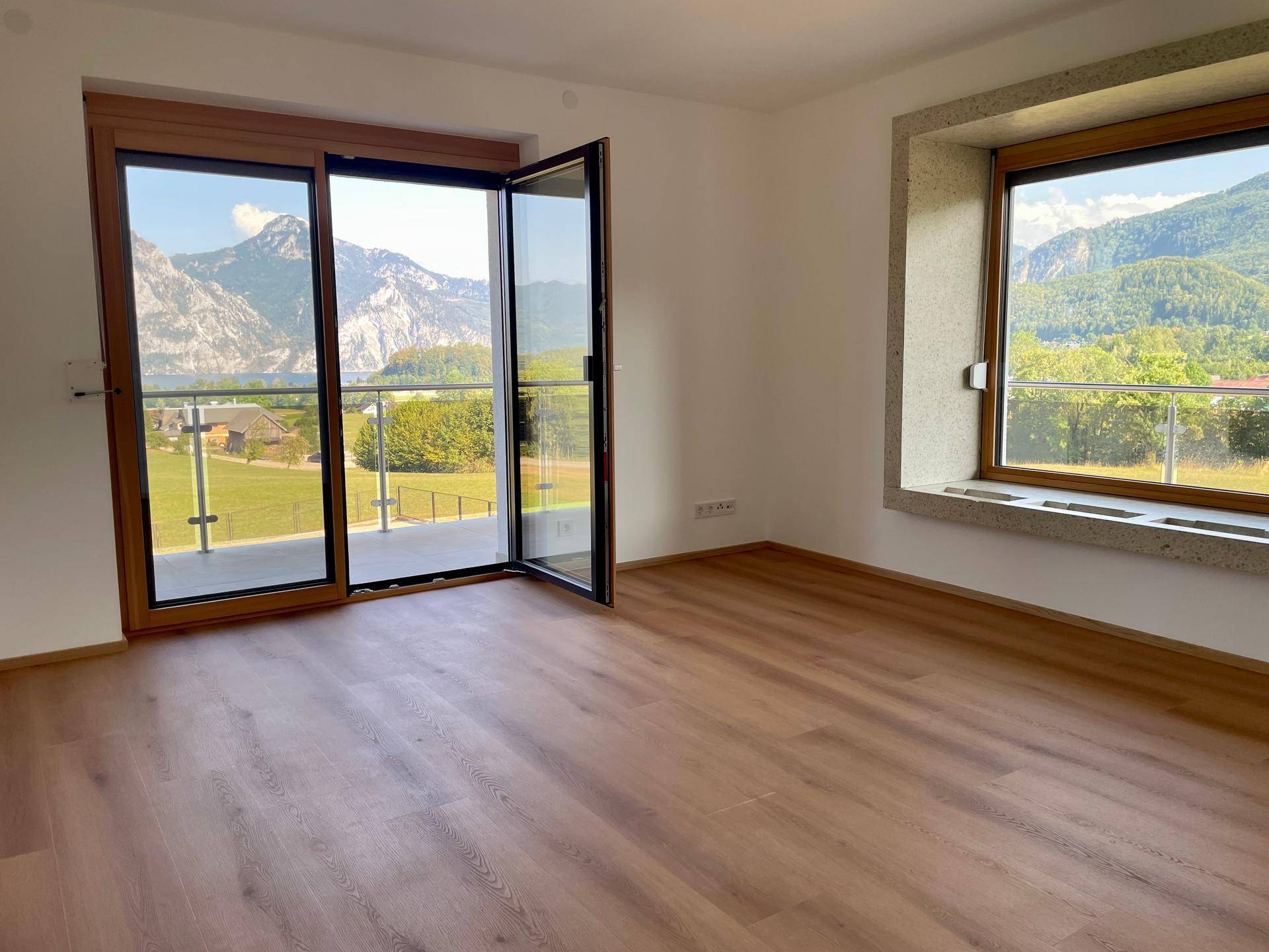 Heller Wohnraum mit Holzboden, großen Fenstern und beeindruckendem Bergblick.