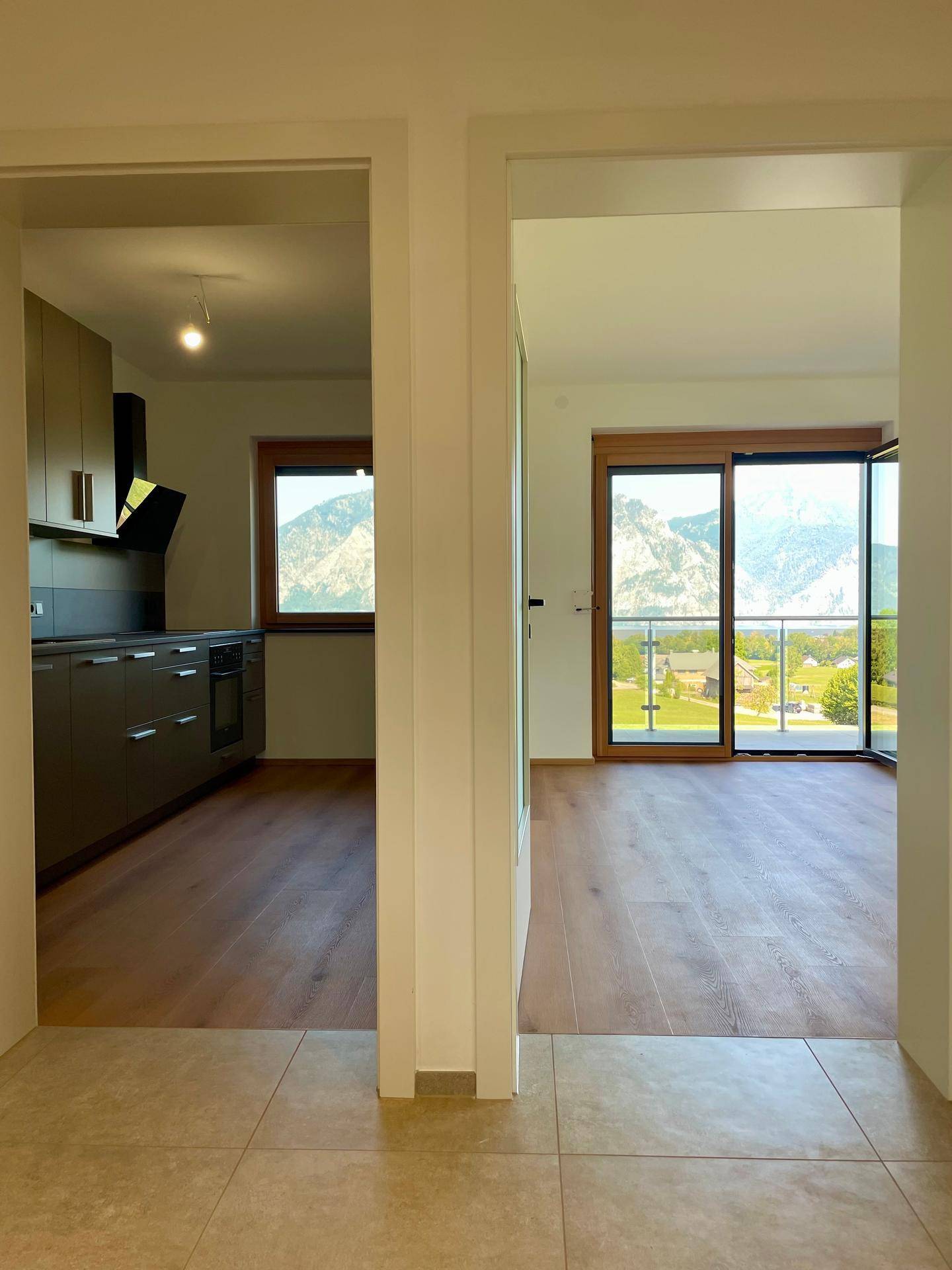 Blick vom Flur in eine moderne Küche und einen hellen Wohnbereich mit Bergblick.
