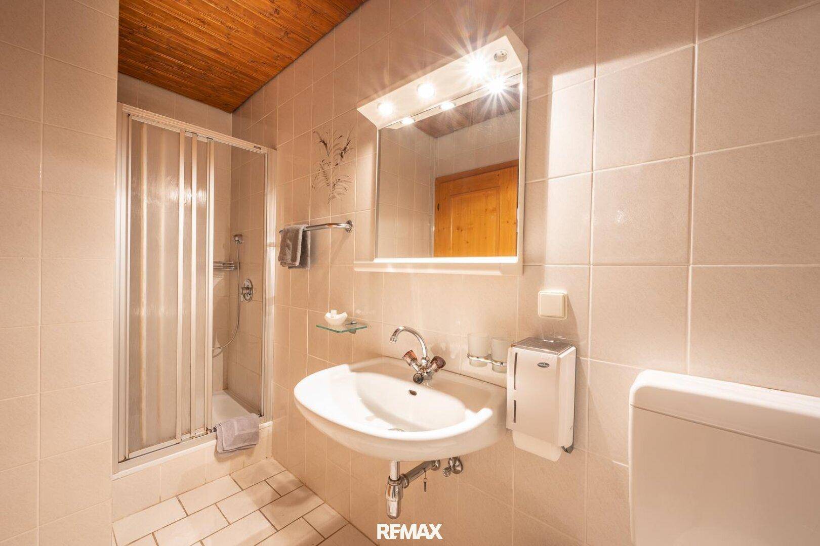 Helles Badezimmer mit beigen Fliesen, Dusche und Einzelwaschbecken.