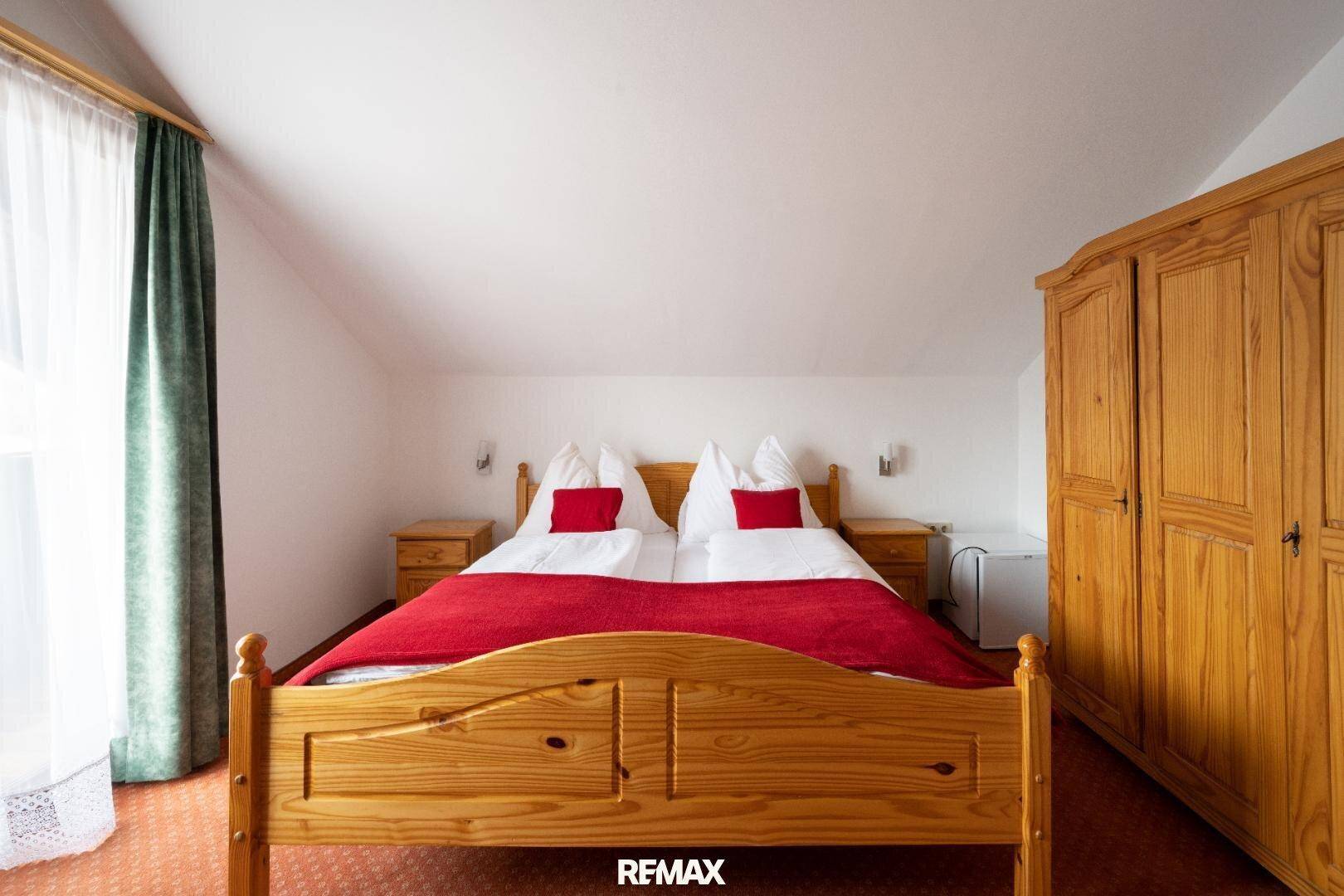 Gemütliches Schlafzimmer mit Doppelbett, Holzschrank und roter Bettwäsche unter Dachschräge.