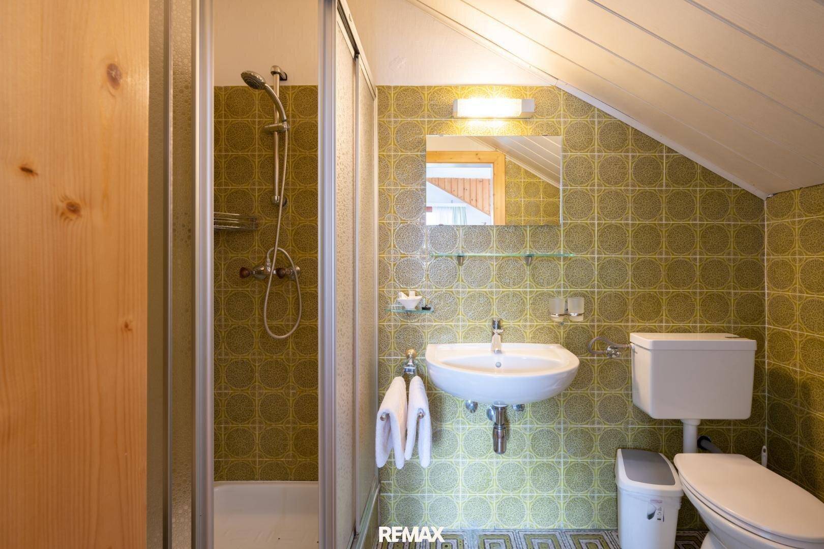 Badezimmer im Retro-Stil mit grünen gemusterten Fliesen, Dusche und Dachschräge.