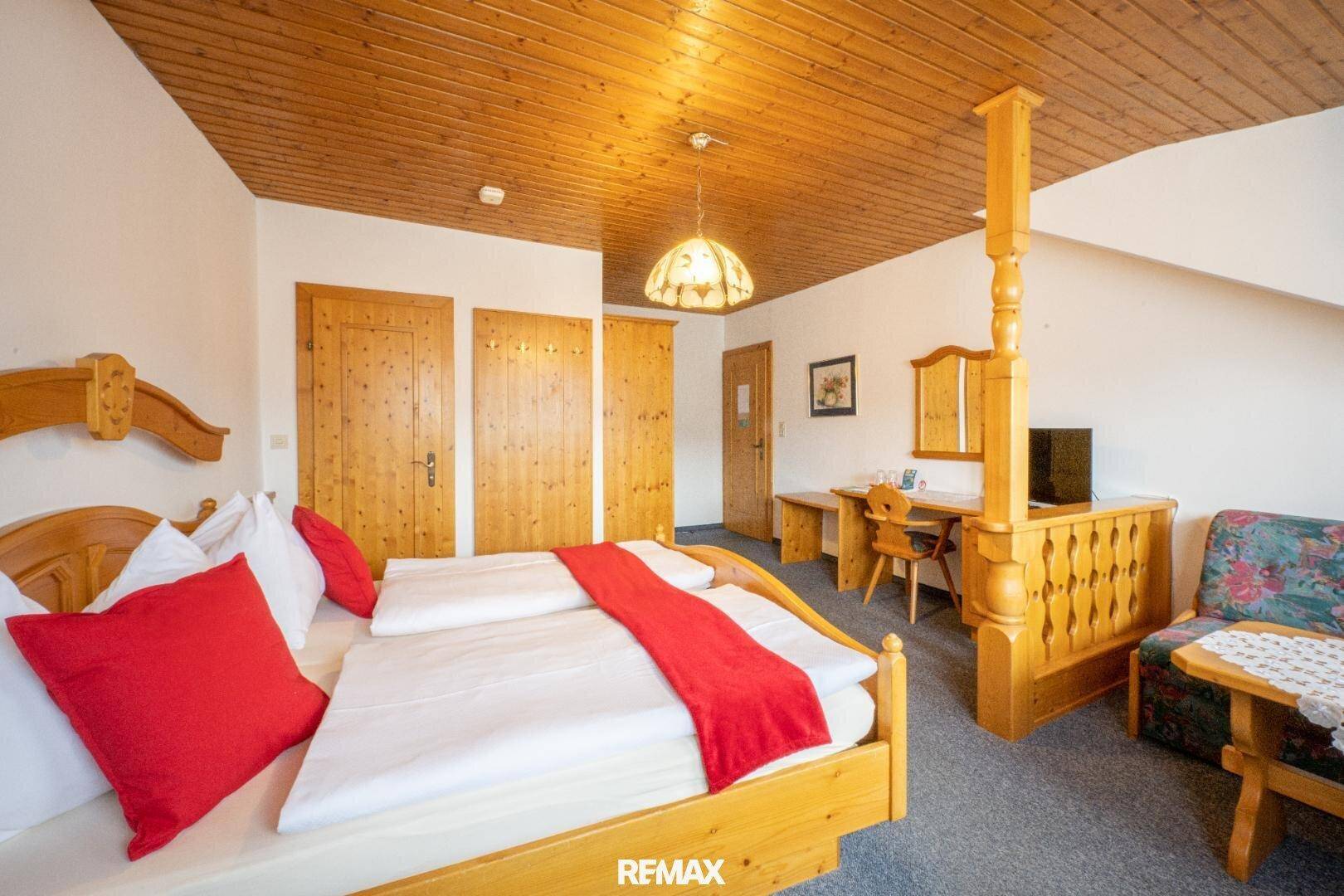 Gemütliches Schlafzimmer im Landhausstil mit Holzbett, Holzdecke und roter Bettwäsche.