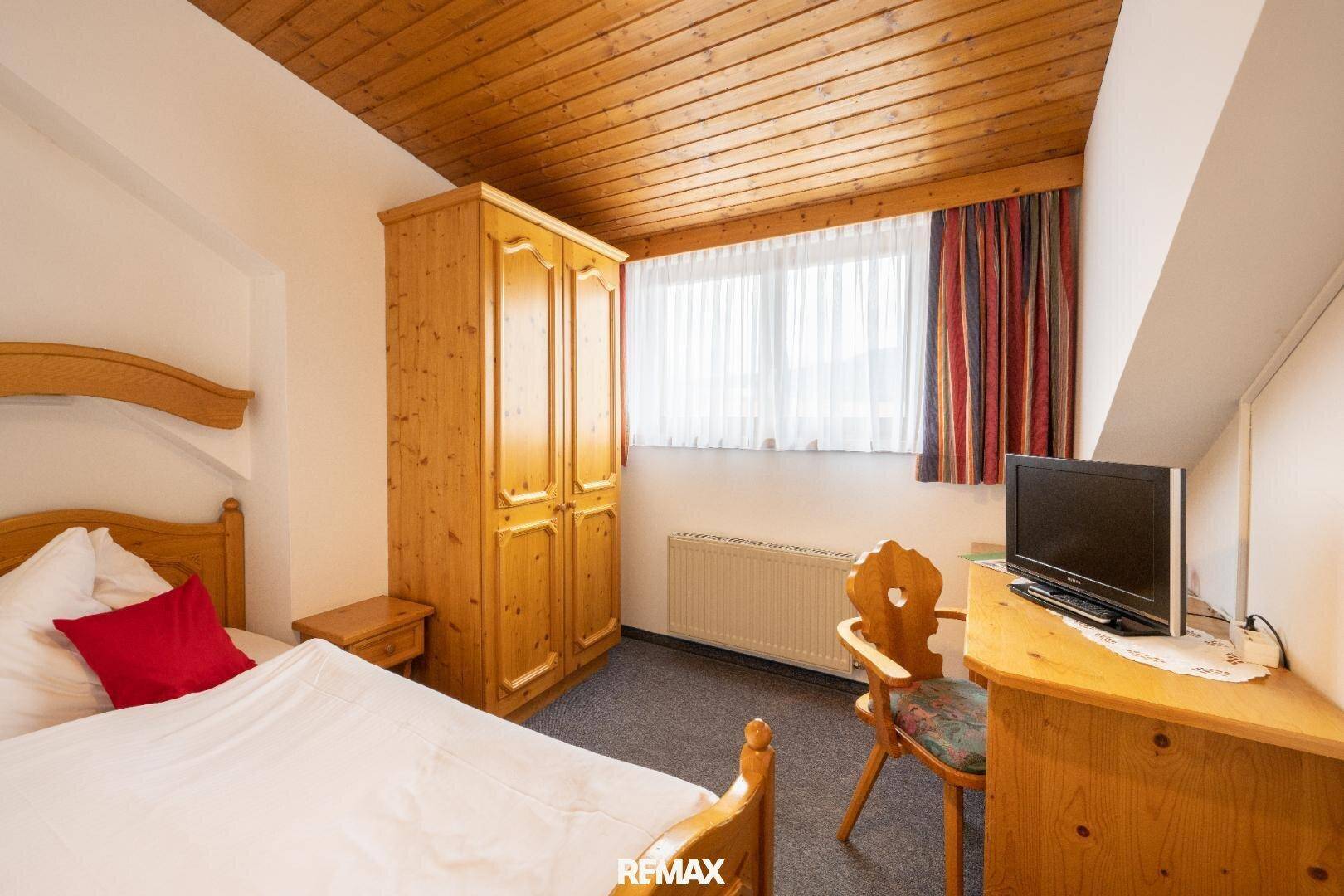 Helles Schlafzimmer mit Holzbett, Kleiderschrank und Fenster mit Vorhängen.