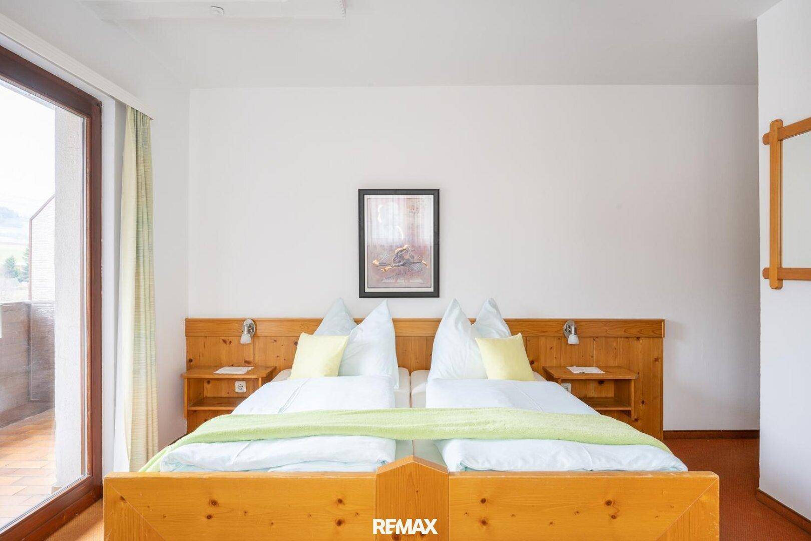 Helles Schlafzimmer mit Doppelbett, Holzmöbeln und Zugang zu einem Balkon.