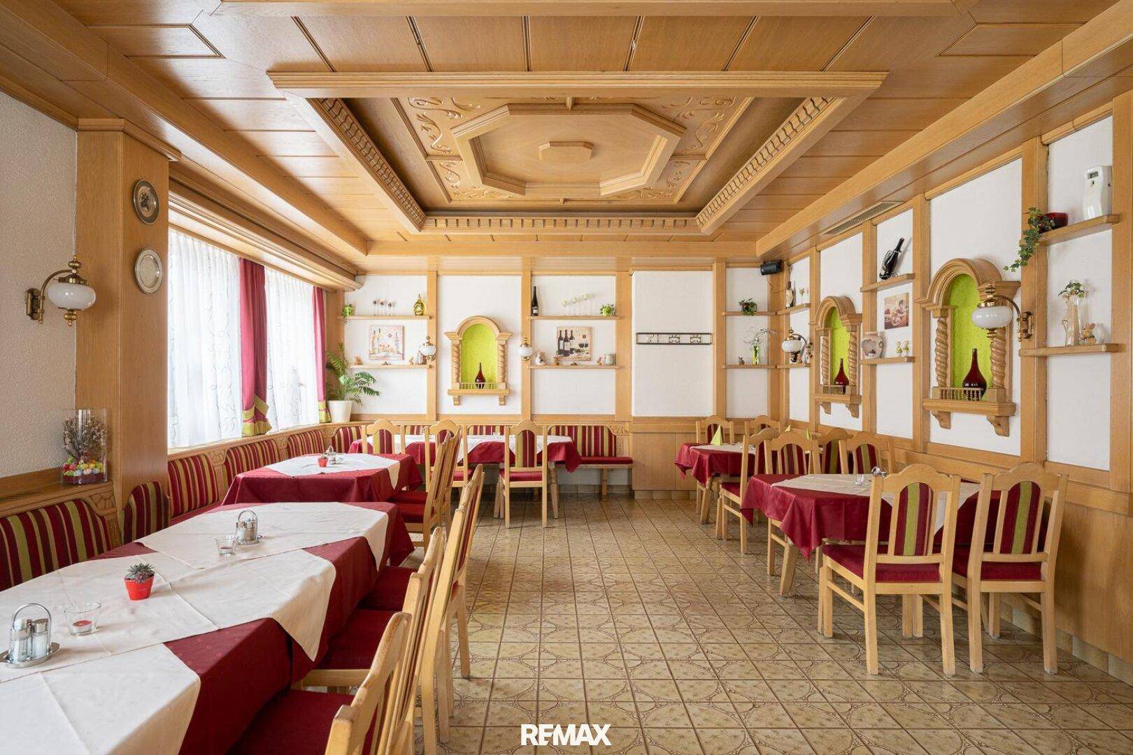 Großer Speisesaal mit Holzvertäfelung, roten Tischdecken und geschnitzter Holzdecke.