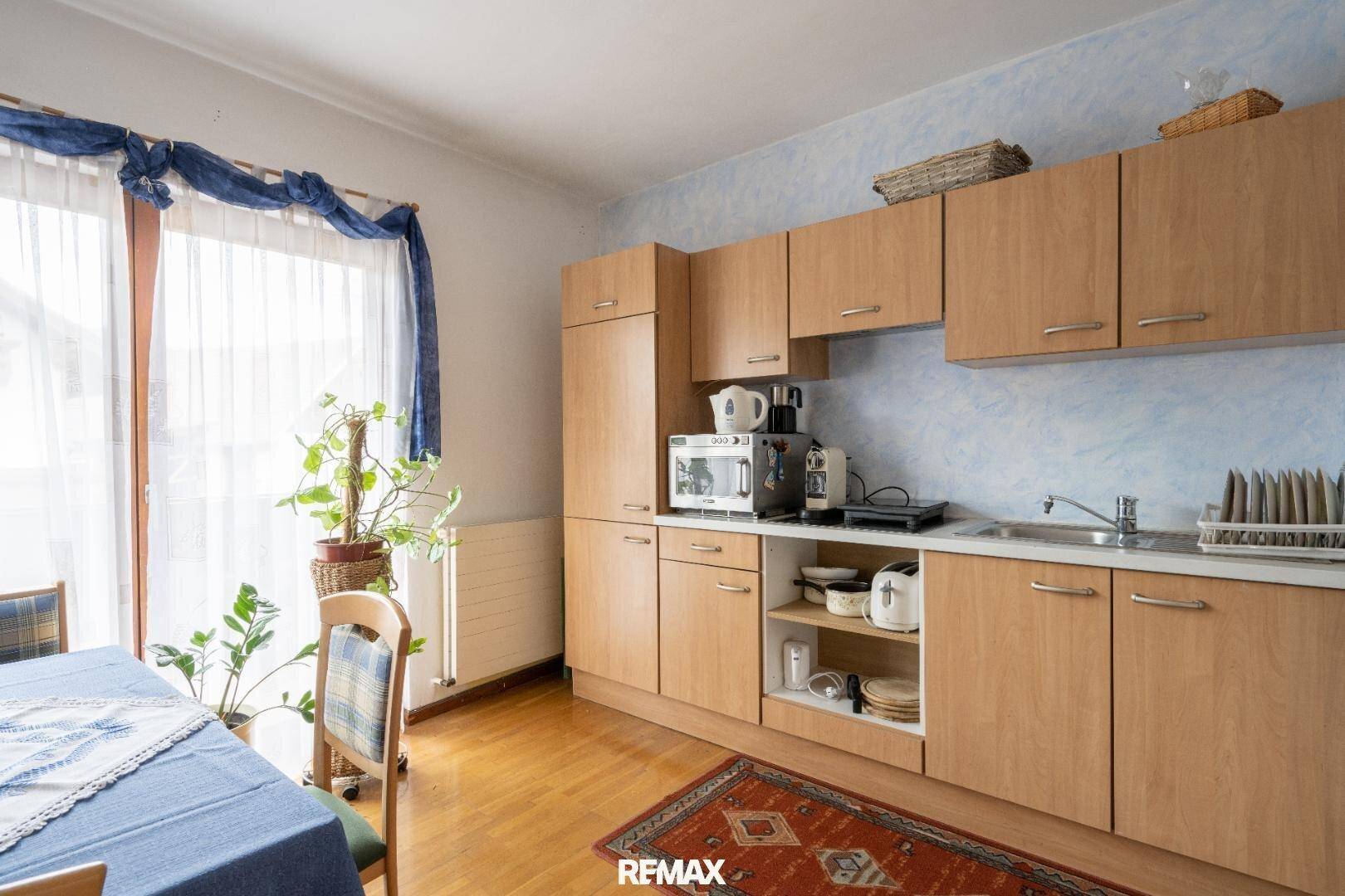 Einfache Küche mit Holzschränken, Esstisch und Zugang zu einem Balkon.