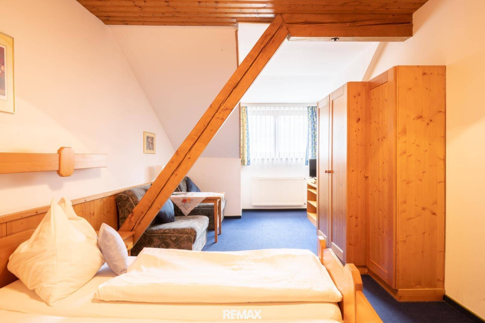 Rustikales Schlafzimmer mit Holzbalken, Einzelbett und blauem Teppichboden.