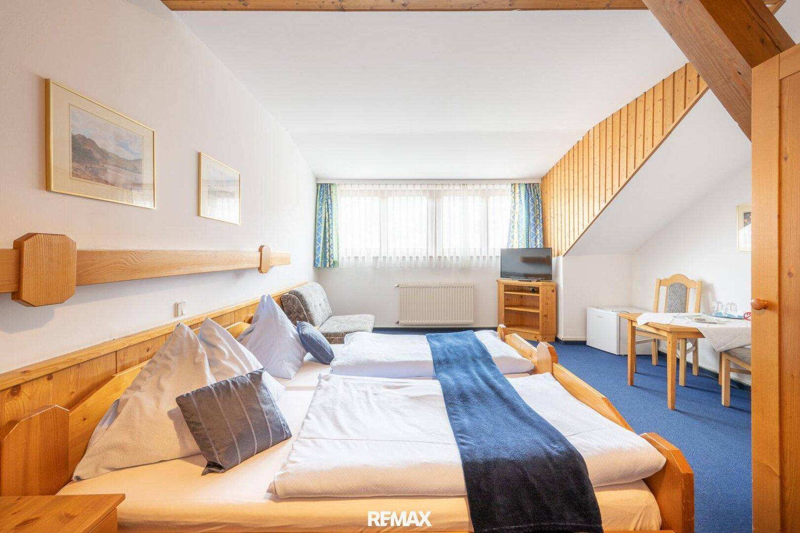 Geräumiges Schlafzimmer mit zwei Einzelbetten, blauem Teppich und Fensterblick.