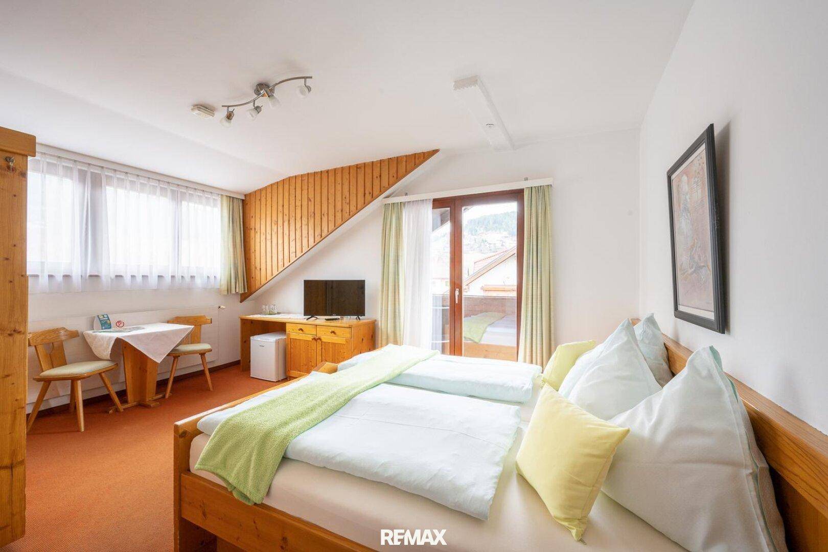 Freundliches Schlafzimmer mit Balkonzugang, zwei Betten und orangefarbenem Teppich.