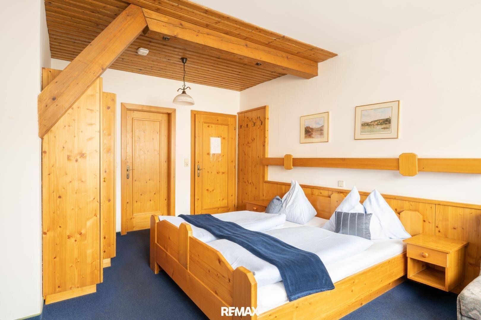 Traditionelles Schlafzimmer mit Holzmöbeln, Holzdecke und blauem Teppichboden.