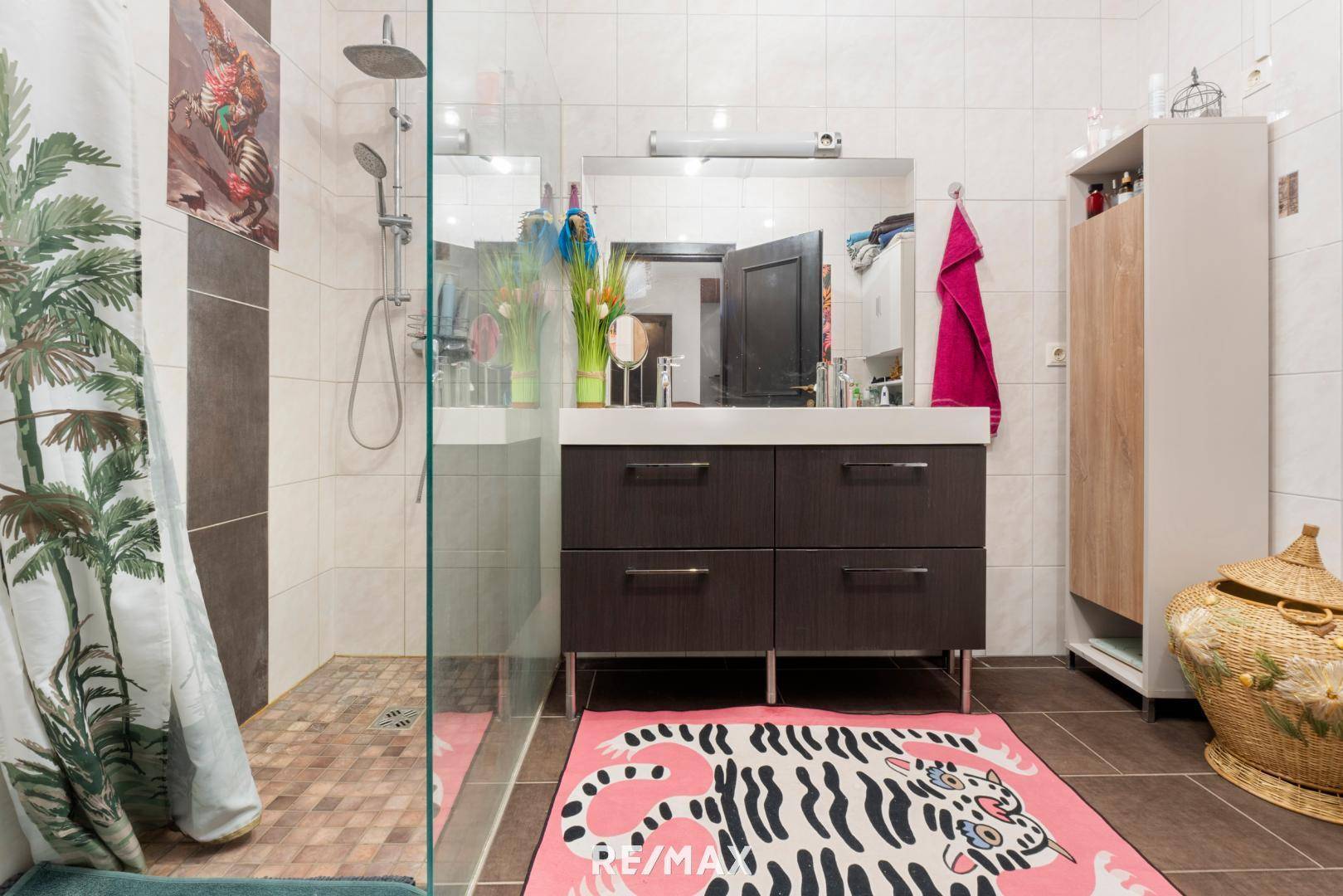 Modernes Badezimmer mit begehbarer Dusche, dunklem Waschtisch und farbenfrohem Teppich.