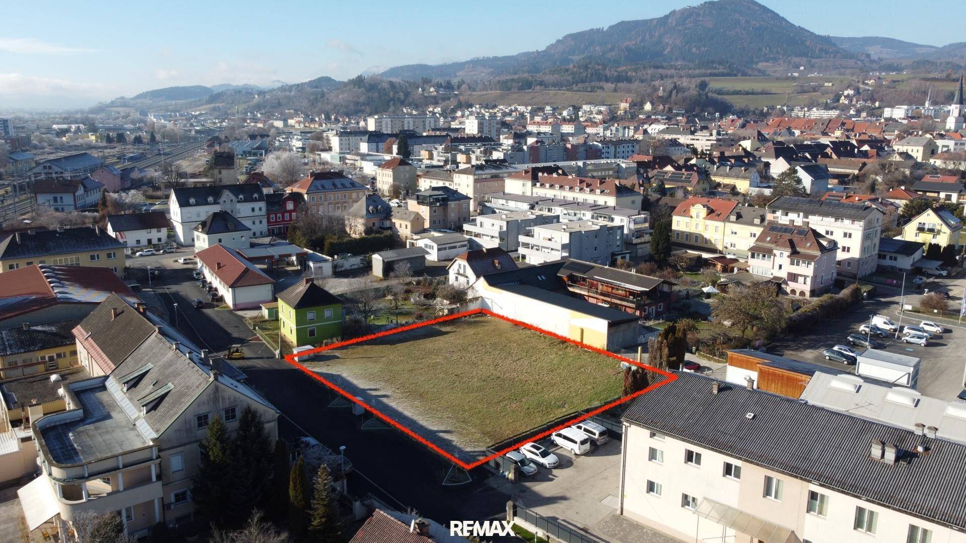 Luftaufnahme eines Baugrundstücks in städtischer Lage mit umliegender Bebauung und Bergblick.