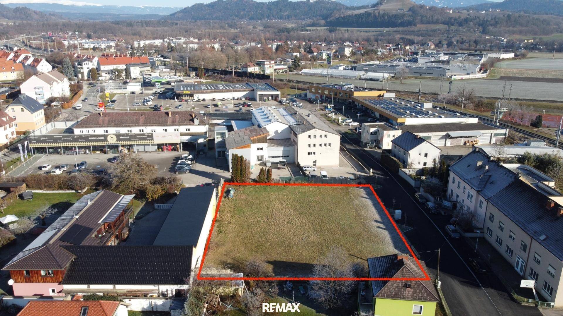 Luftaufnahme eines Baugrundstücks in einer Mischzone mit Blick auf umliegende Gebäude und Berge.