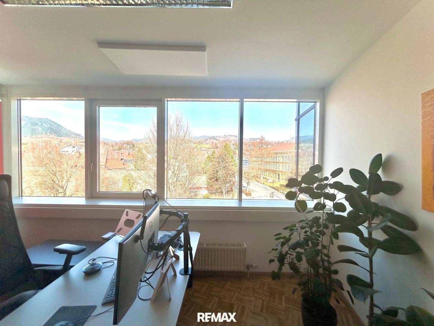 Büroarbeitsplatz mit großem Fenster und Ausblick auf die umliegende Landschaft und Gebäude.