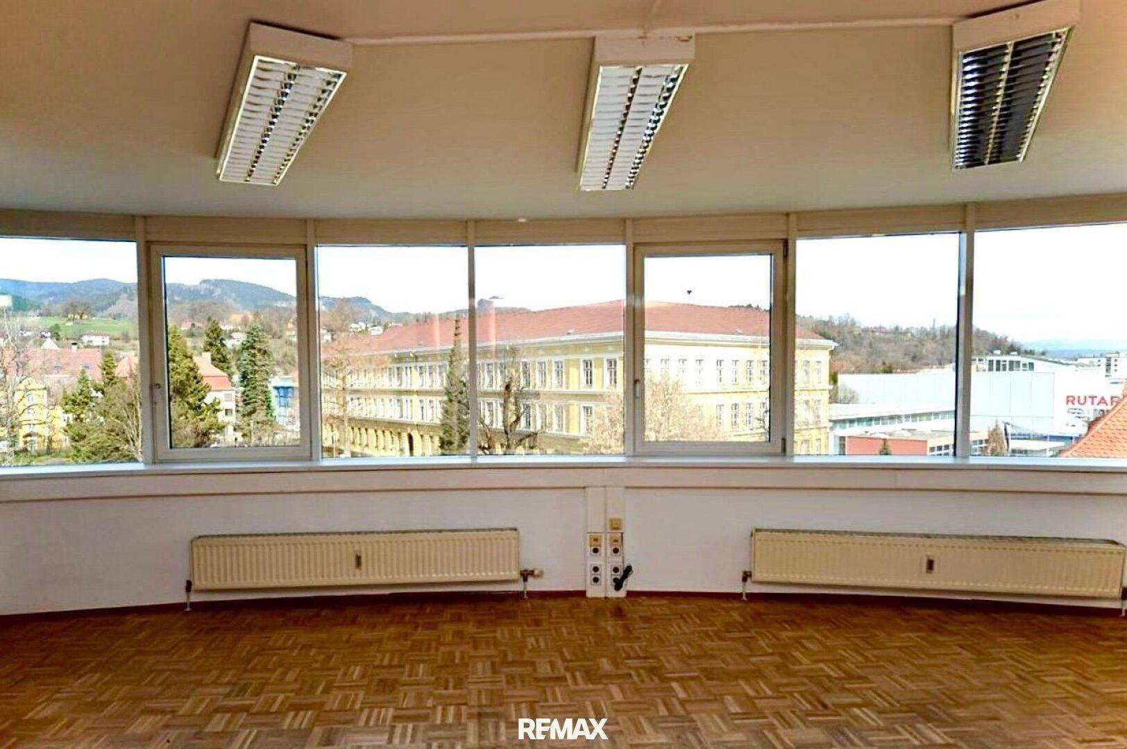 Leeres Büro mit Parkettboden und einer geschwungenen Fensterfront mit Stadt- und Landschaftsblick.