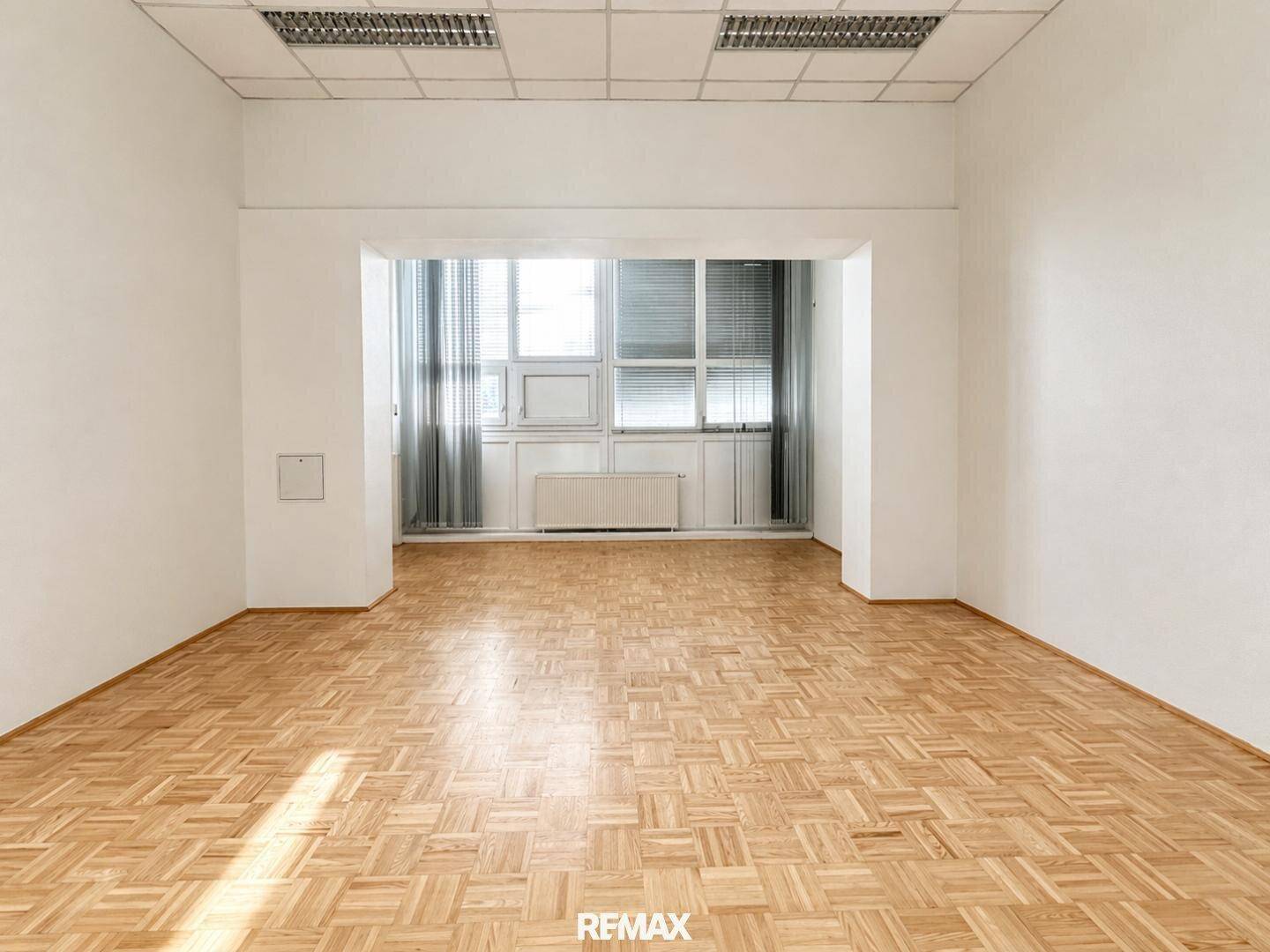 Heller Büroraum mit Parkettboden und großen Fenstern, die viel Tageslicht hereinlassen.