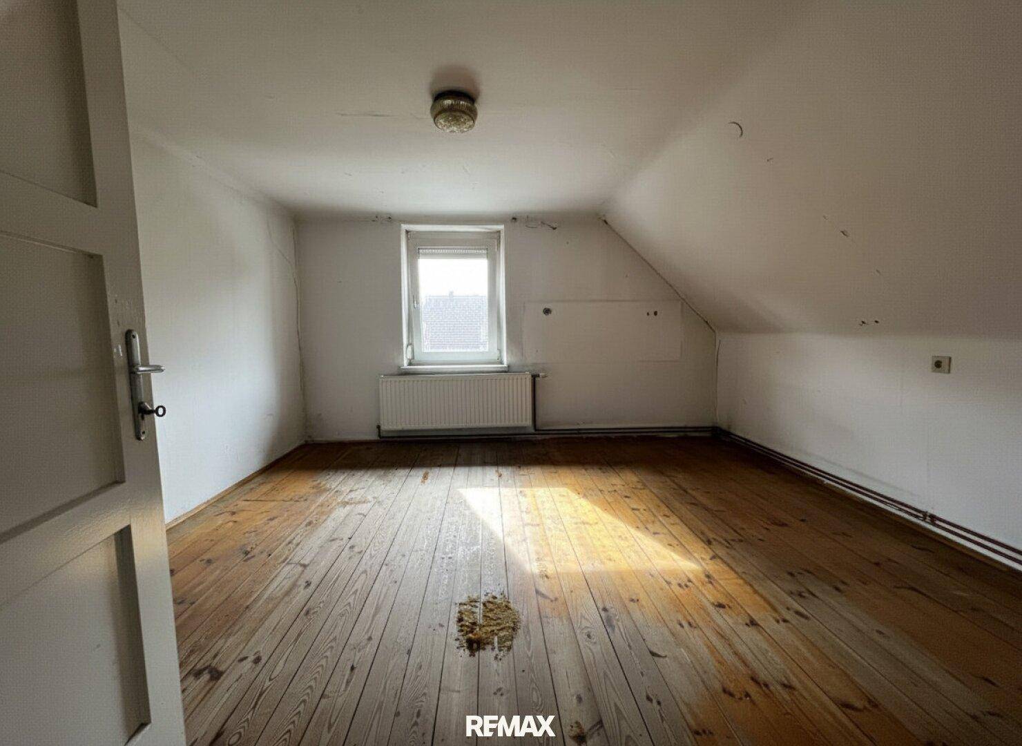 Dachzimmer mit schräger Decke, Holzdielenboden und einem Fenster, das den Raum erhellt.