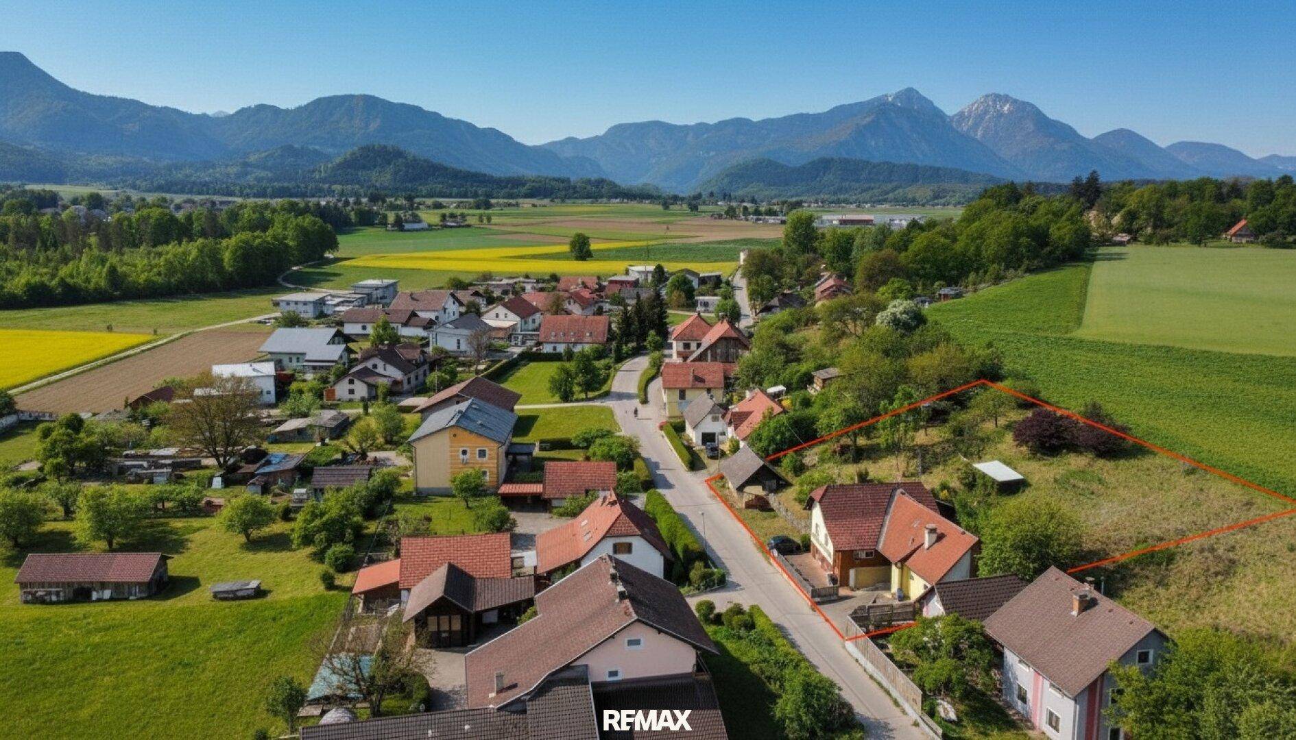 Panoramablick aus der Luft auf ein Wohngebiet mit weiten Feldern und majestätischen Bergen am Horizont.