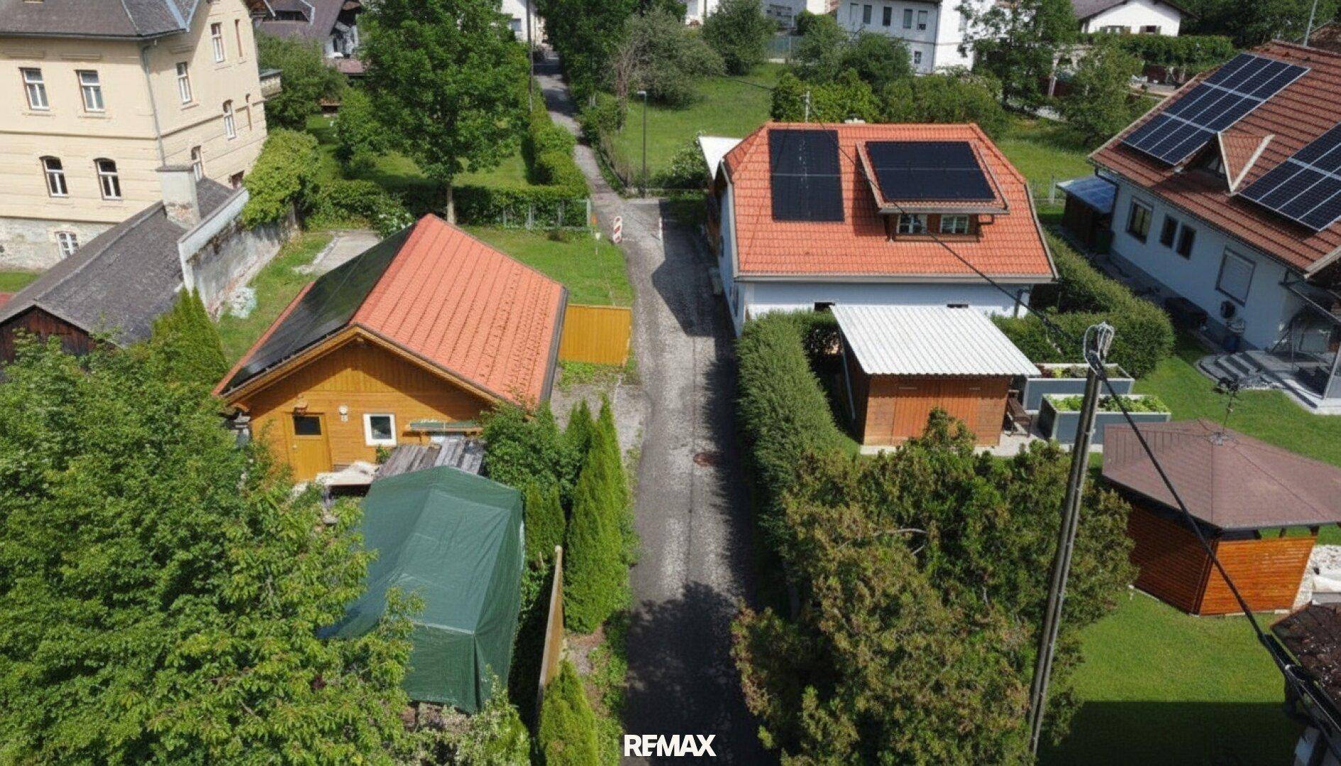 Vogelperspektive auf zwei Wohnhäuser mit Zufahrt, gepflegten Hecken und Solarmodulen auf den Ziegeldächern.