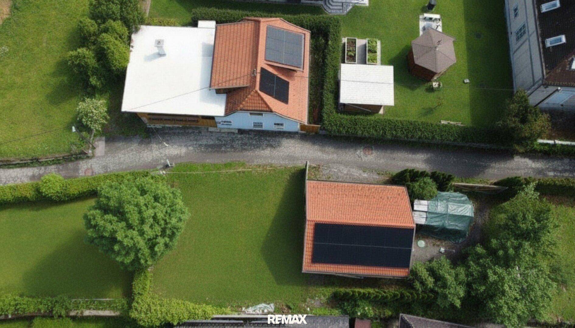 Draufsicht auf ein Wohngebiet mit Häusern, weitläufigen Rasenflächen, Solaranlagen und einem Gartenpavillon.