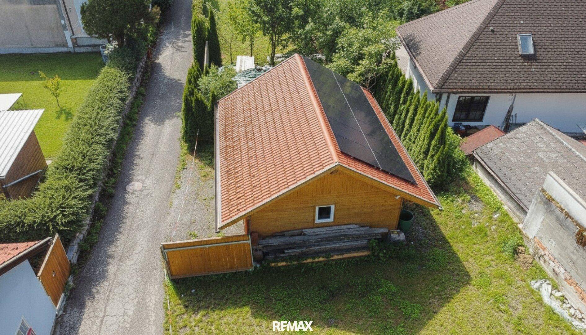 Luftaufnahme eines Holzhauses mit Ziegeldach und Solaranlagen, umgeben von einer grünen Hecke und Zufahrt.