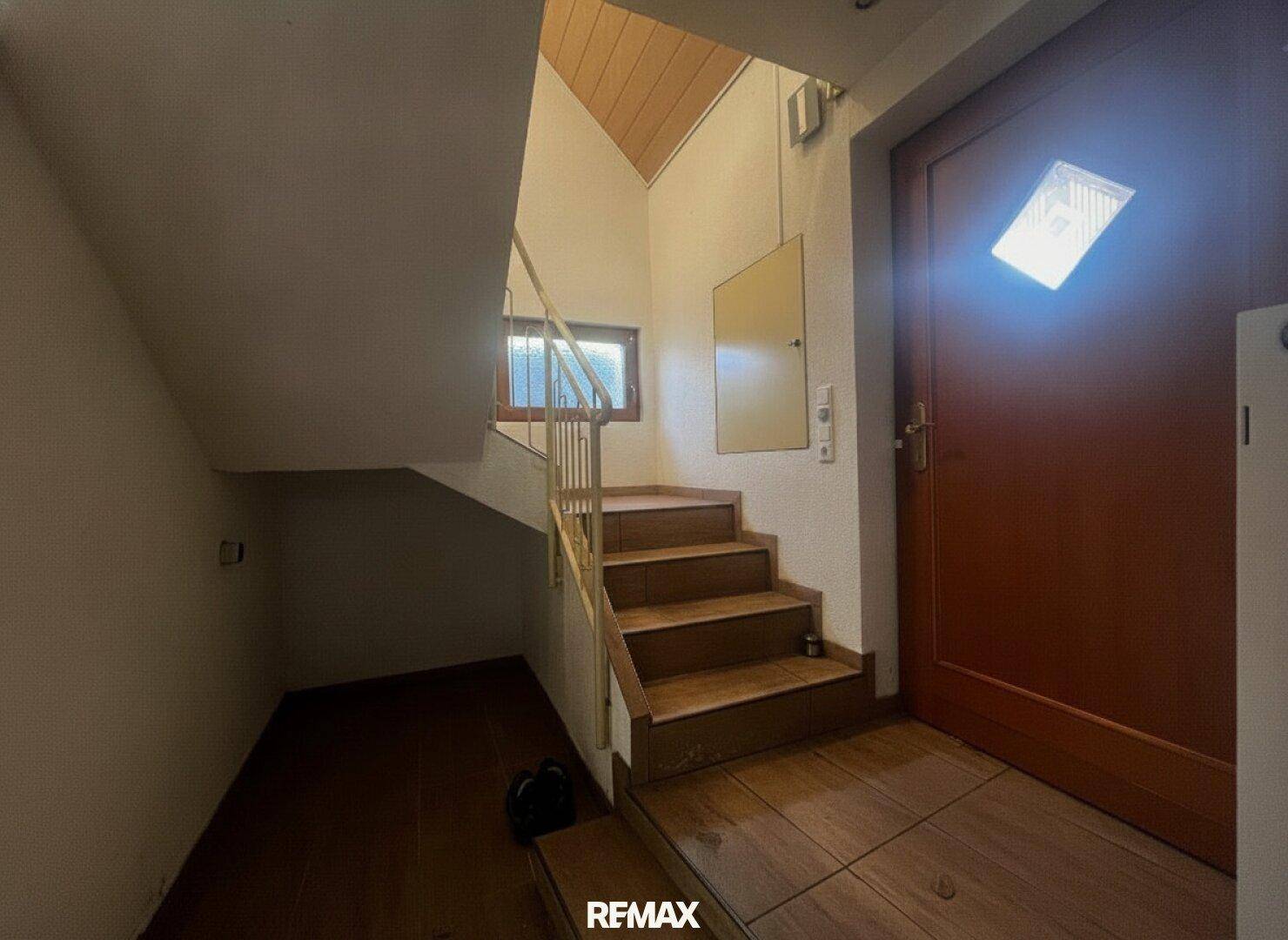Eingangsbereich mit Treppe, Holztür und gefliestem Boden, der zu den oberen Etagen führt.
