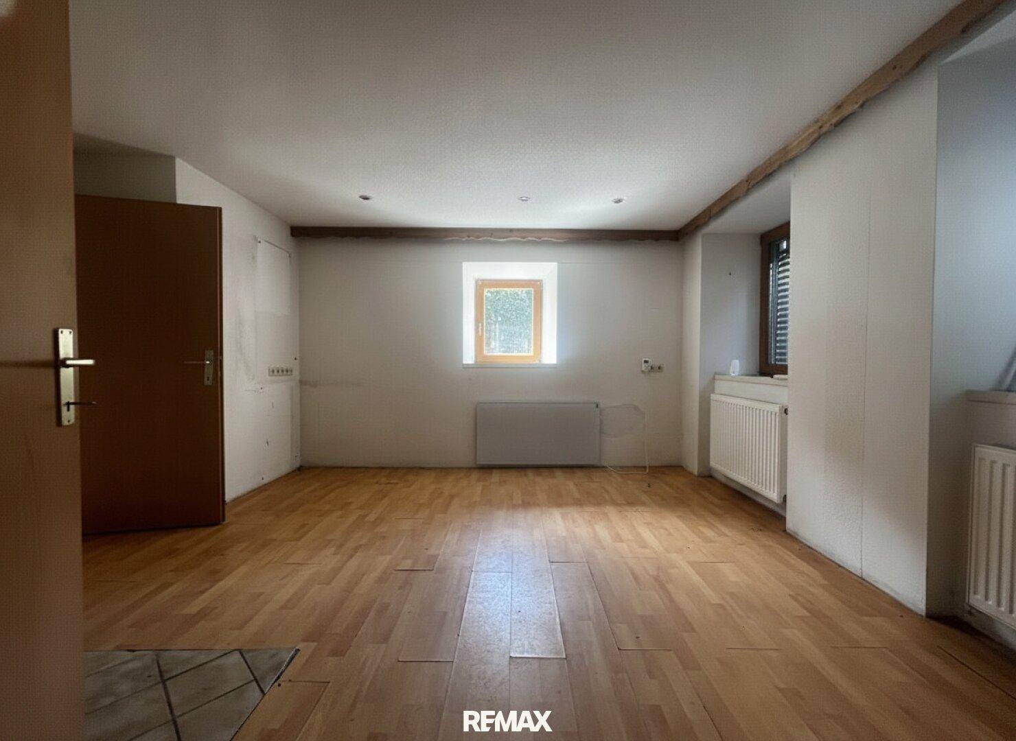 Leeres Zimmer mit hellem Holzfußboden, weißen Wänden und einem kleinen Fenster, bereit zur individuellen Gestaltung.