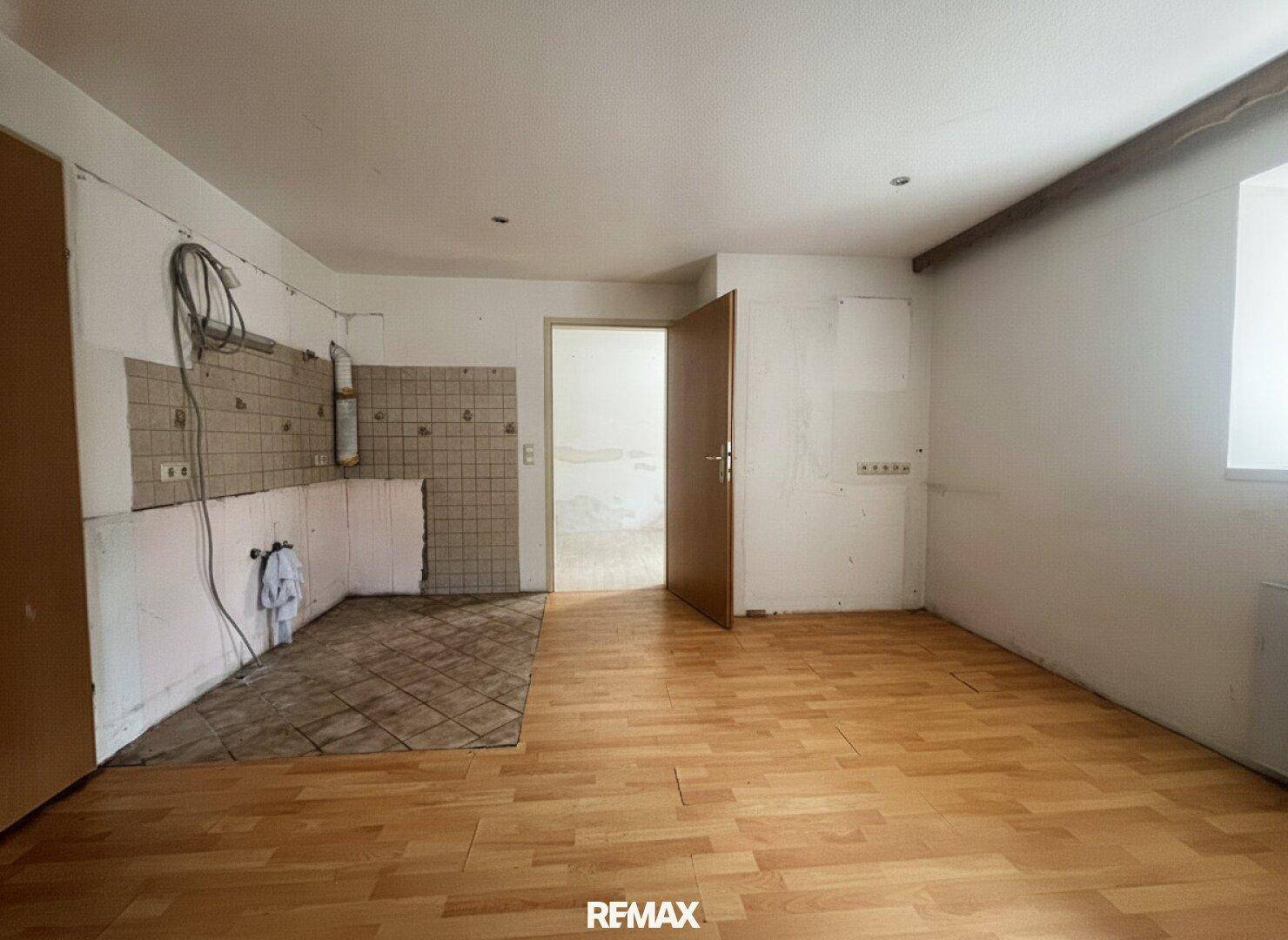 Raum für eine Küche mit Holzfußboden, vorbereiteten Wänden und Anschlüssen für die Kücheninstallation.