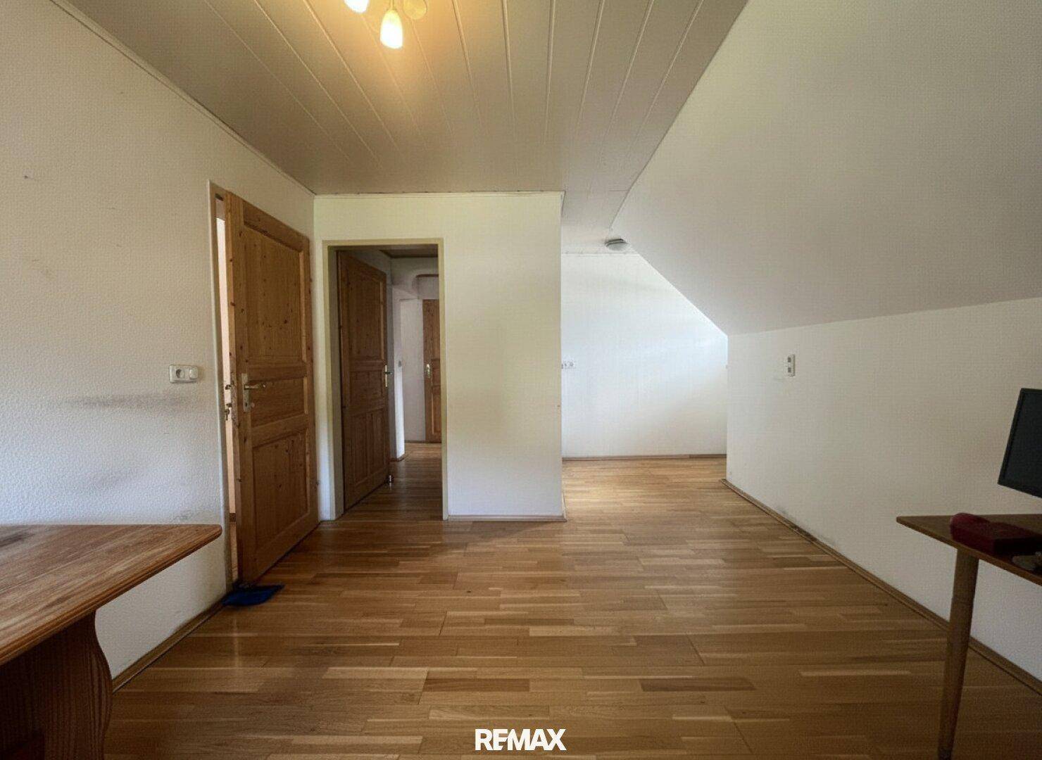 Geräumiger Dachbodenraum mit Holzfußboden, weißen Wänden und schräger Decke, bietet Ausbaupotenzial.