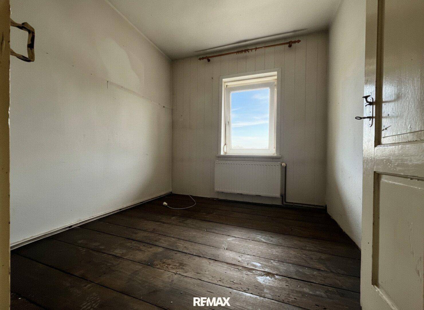 Kleiner Raum mit dunklem Holzdielenboden und einem Fenster, das Tageslicht hereinlässt.