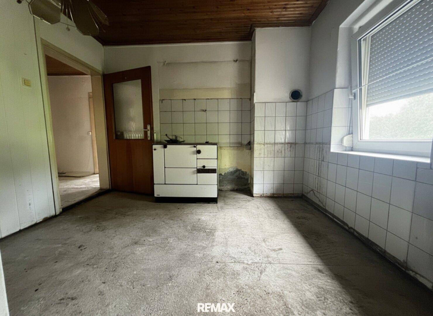 Alte Küche mit Fliesenwänden, Betonboden und einem traditionellen Ofen, renovierungsbedürftig.