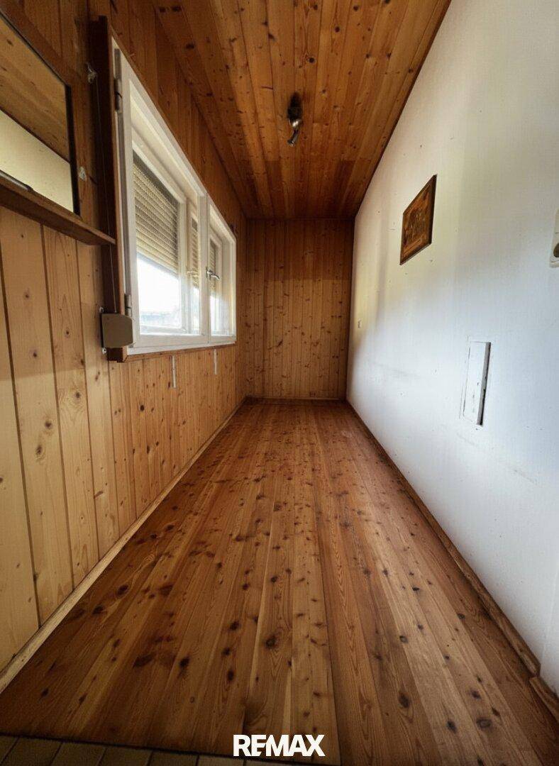 Langer Raum mit Holzwänden, Holzdecke und Holzdielenboden, hell durch ein großes Fenster.